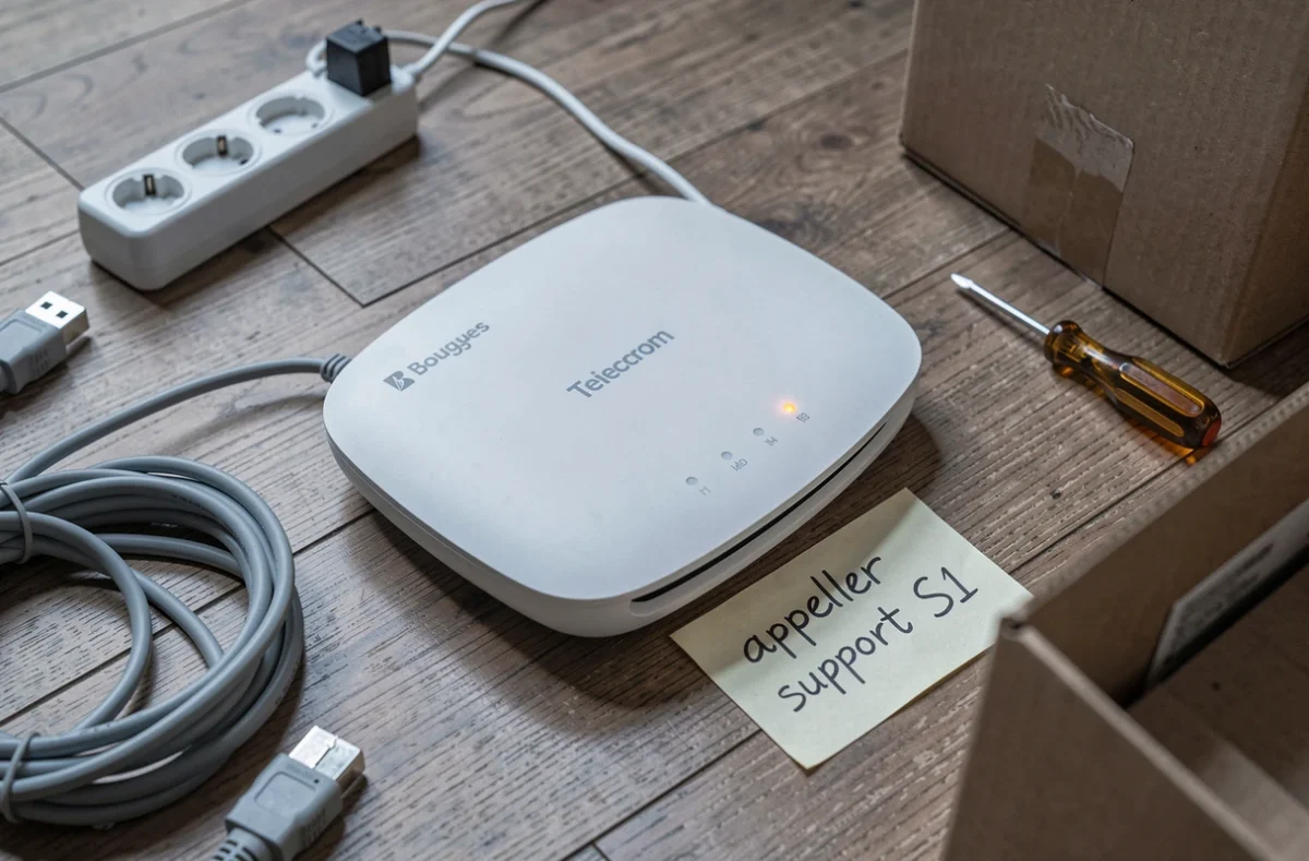Gros plan d'un routeur Bouygues posé sur un parquet avec un câble ethernet et une note manuscrite mentionnant le code erreur S1 lors d'une installation après déménagement